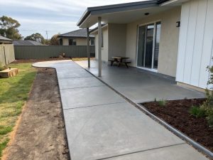 Concrete path and patio running alongside a house, with an outdoor table
